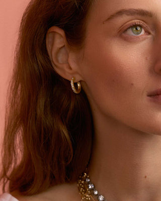 Close-up of a model wearing gold hammered hoop earrings with pave diamonds